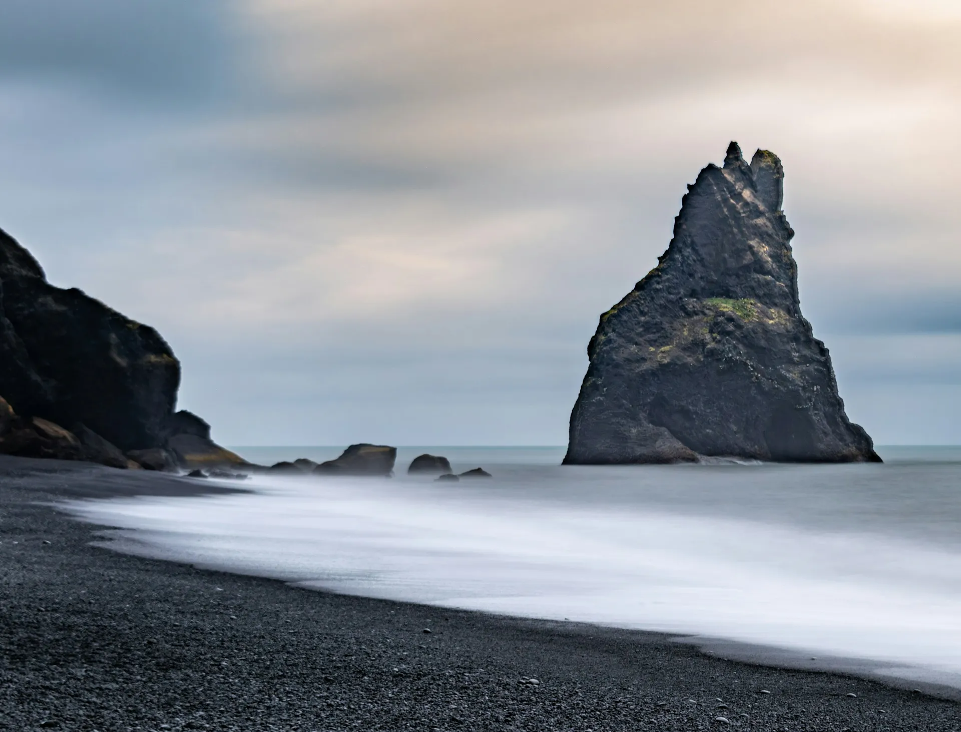 Plage de sable noir islandaise sous une lumière dorée froide, brume sur l'océan